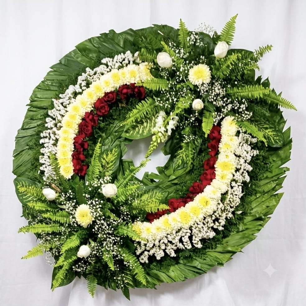 Corona de flores funeraria de forma circular con un diseño clásico de rosas rojas y amarillas, crisantemos blancos y verdes follaje de helecho, ideal para mostrar condolencias.